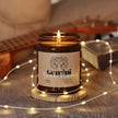 Gemini Soy Candle in amber jar with lit wick, surrounded by soft lighting and a cozy setting for astrology lovers.