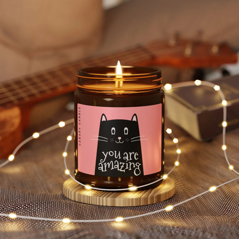 Amazing Soy Candle in amber jar with playful cat label, surrounded by warm lights and a cozy atmosphere.