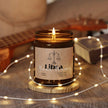Libra Soy Candle in amber jar with warm glow, placed on a wooden base, surrounded by soft light.
