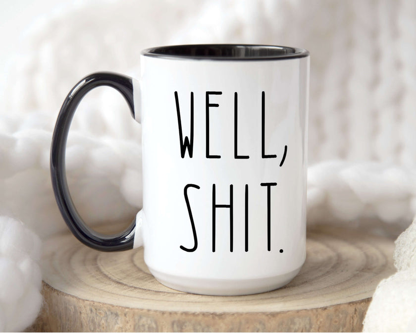 Sarcastic coffee mug with hand-lettered phrase 'Well, Shit.' in black on white ceramic with a colored handle.