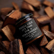 Scented soy candle in amber jar, perfect for a funny coworker gift, surrounded by hardwood pieces.